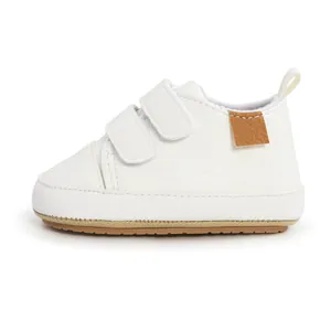 Close-up side view of white baby walking shoe featuring double Velcro straps and tan sole