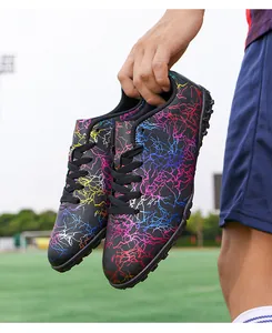 Gros plan de chaussures de foot noires à motifs éclair colorés sur un terrain de sport.