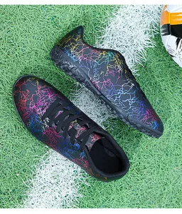 Vue détaillée de chaussures de foot à motif craquelé coloré sur gazon synthétique.