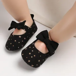Nahaufnahme von schwarzen Baby-Prinzessin-Schuhen mit goldenen Sternen und Schleife.