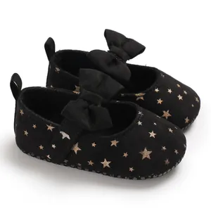 Detailaufnahme schwarzer Baby-Prinzessinenschuhe mit goldenen Sternen und Schleifen.