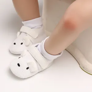 Nahaufnahme von weißen Lauflernschuhen für Babys mit einem süßen Bärengesicht und weichem Strick