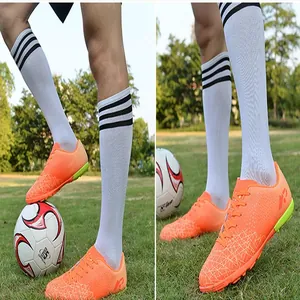 Detail shot of orange youth soccer shoes with turf studs on artificial grass.