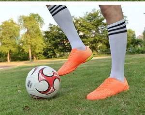 Action shot of vibrant orange turf soccer shoes on green grass with a football detail