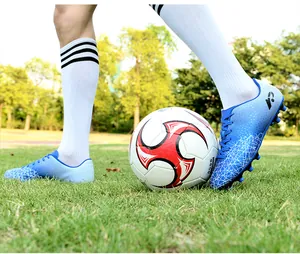 Professional blue youth soccer cleats on green turf field next to a soccer ball.