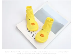 Close-up of yellow duckling pattern baby walker socks with non-slip soles on minimalist prop.