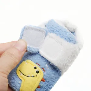 Detail van een zachte pluchen babyschoen met klittenband en een gele dinosaurus