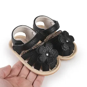 Close-up of black baby sandals with flower detail held in hand to show size
