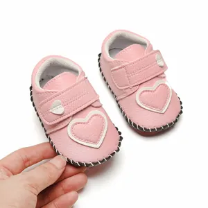 Gros plan d'une main tenant des chaussures bébé roses avec motif de cœur