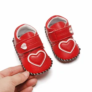 Main tenant une chaussure de bébé rouge avec un cœur blanc et une semelle très souple