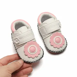 Gros plan sur chaussures bébé blanches souples avec fleur rose et semelle en caoutchouc