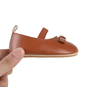 Détail en gros plan d'une chaussure marron pour bébé fille avec nœud et sangle élastique.