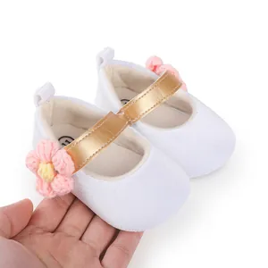 Detailed view of white baby walking shoes featuring a gold strap and pink flower