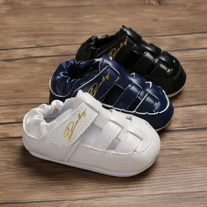 Close-up view of white, navy, and black faux leather closed-toe baby sandals with Baby script