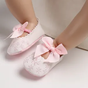 Gros plan de chaussures bébé princesse blanches avec un grand nœud rose et broderies