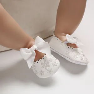 Détail des chaussures de princesse blanches pour bébé avec broderie et gros nœud