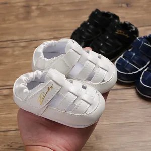Close-up of white baby closed-toe sandals with gold Baby script and velcro strap.