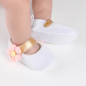 Close-up of white baby walker shoes with gold strap and pink crochet flower detail.