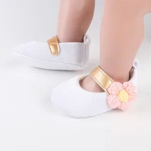 Close-up view of white baby toddler shoes featuring a gold strap and pink crochet flower