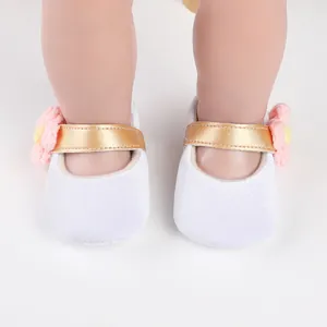 Close-up of white baby girl princess shoes with gold strap and pink flower detail
