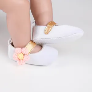 Detail view of white baby princess shoes with pink knit flower and gold strap