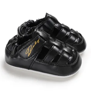 Close-up detail of black leather baby sandals with gold Baby script on strap