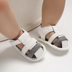 Close-up detail of white and grey soft-soled baby summer sandals worn on infant feet.