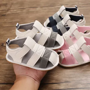 Close-up of soft-sole baby summer sandals in multiple colors held by hand for scale.