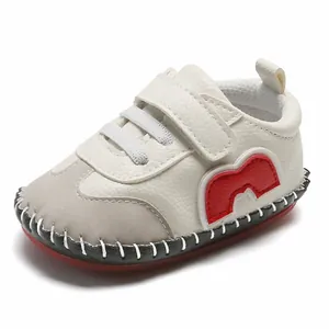 Gros plan d'une chaussure de bébé à semelle souple en cuir blanc avec détails rouges.