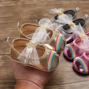 Close-up of baby girl gold pre-walker shoe with rainbow toe and white mesh bow detail.