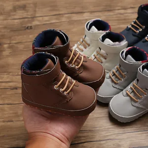 Detailed view of brown high-top soft sole baby walking shoes held by hand on wood.