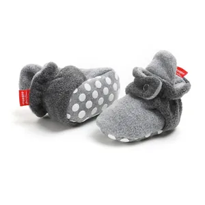 Close-up of grey fleece baby booties with anti-slip polka dot soles and red logo tag