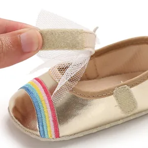 Close-up of gold baby walker shoe showing velcro strap with tulle bow and rainbow embroidery.