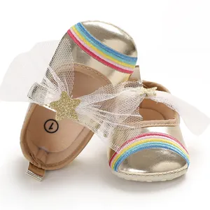 Close-up of golden baby walker shoes with white mesh bow, glitter star, and rainbow toes