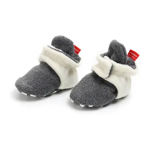 Close-up detail of grey baby fleece booties with white plush cuff and red brand tag