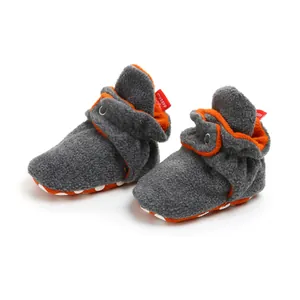 Close-up of warm gray and orange fleece baby booties with soft anti-slip soles.