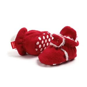 Detail view of red plush winter baby shoes with white faux fur trim and polka dot soles.