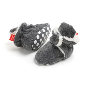 Close-up of grey fleece winter baby booties with white plush lining and non-slip polka dot soles.