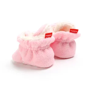 Close-up of pink plush baby booties with soft white lining and red logo label