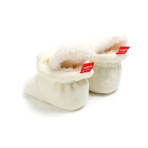 Detail view of the fuzzy cream winter baby booties featuring soft fleece and red brand tags