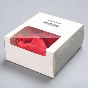 Red plush baby shoes shown inside a premium white cardboard display box with clear window