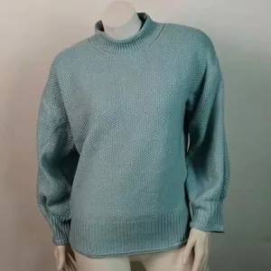 Primer plano de un suéter de punto grueso azul verdoso con cuello alto y mangas de linterna.