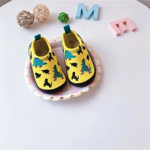 Close-up of yellow children's canvas shoes with dinosaur patterns on a white background.