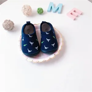 Detail view of navy blue dinosaur print baby slip-on canvas walking shoes on a plate