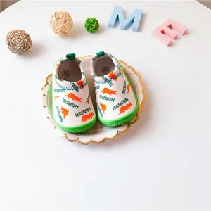 Detailed shot of kids white slip-on canvas shoes featuring orange dinosaur prints