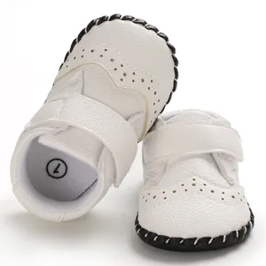 Close-up detail of white handmade baby pre-walker shoes with brogue pattern