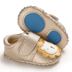 Detailansicht goldener Babyschuhe mit Cartoon-Löwen-Motiv und blauen Anti-Rutsch-Sohlen.