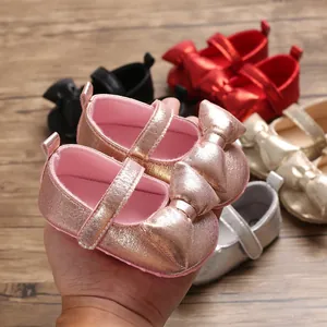 Macro view of shiny rose gold baby princess shoes featuring a large metallic bow decoration.