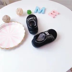 Detailed top view of black toddler canvas slip-on shoes with white stitching on white table