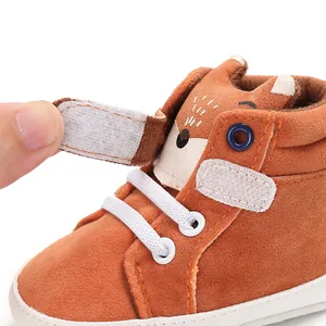 Dettaglio di scarpa per neonati in pelle scamosciata arancione con velcro e design volpe.